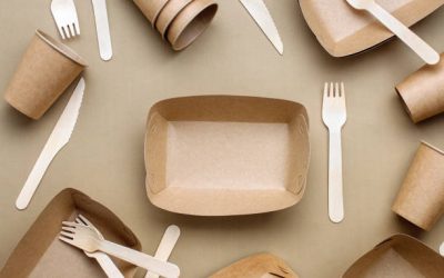 Disposable eco friendly food packaging. Brown kraft paper food containers, forks and knifes on beige background. Top view, flat lay.